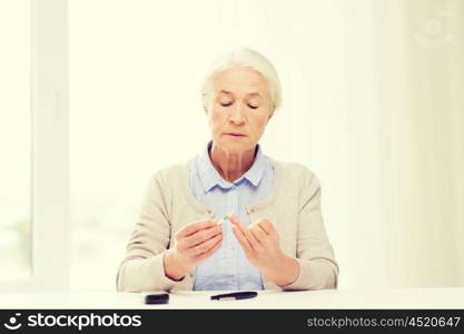 medicine, age, diabetes, health care and people concept - senior woman with glucometer checking blood sugar level at home