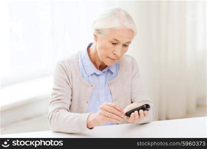 medicine, age, diabetes, health care and people concept - senior woman with glucometer checking blood sugar level at home