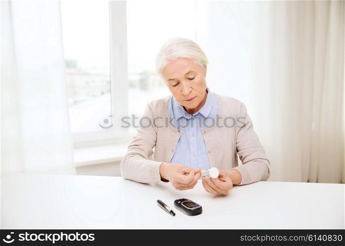 medicine, age, diabetes, health care and people concept - senior woman with glucometer and test stripes checking blood sugar level at home