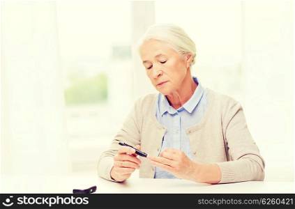 medicine, age, diabetes, health care and people concept - senior woman with glucometer checking blood sugar level at home