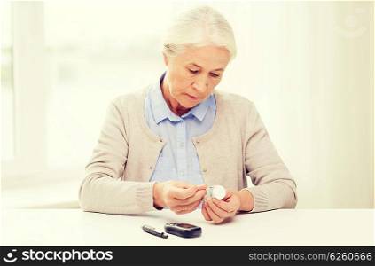 medicine, age, diabetes, health care and people concept - senior woman with glucometer and test stripes checking blood sugar level at home