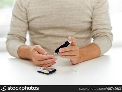 medicine, age, diabetes, healthcare and old people concept - senior man with glucometer checking blood sugar level at home