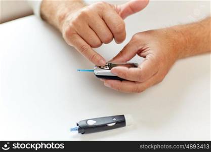 medicine, age, diabetes, healthcare and old people concept - senior man with glucometer checking blood sugar level at home