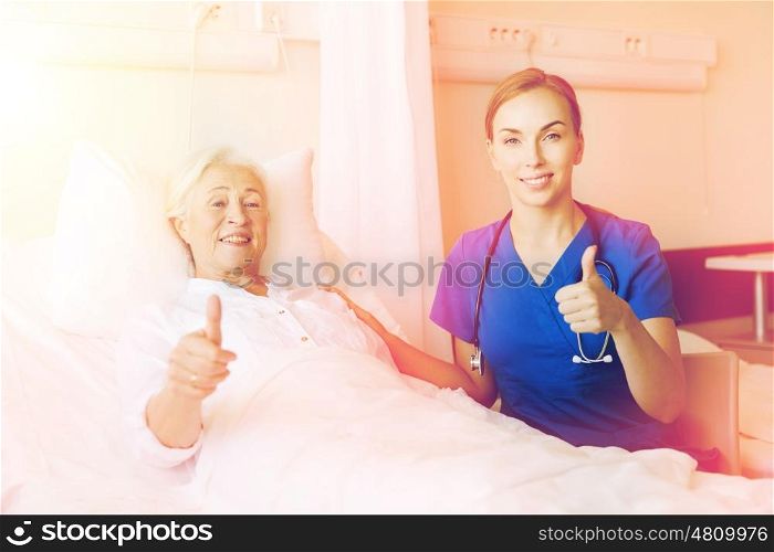 medicine, age, gesture, health care and people concept - doctor or nurse visiting senior woman and showing thumbs up at hospital ward