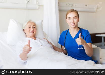 medicine, age, gesture, health care and people concept - doctor or nurse visiting senior woman and showing thumbs up at hospital ward