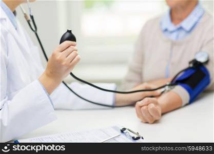 medicine, age, health care and people concept - close up of doctor with tonometer checking senior woman blood pressure level at hospital