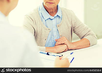 medicine, age, health care and people concept - close up of senior woman and doctor hands with clipboard meeting in medical office