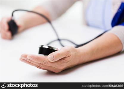 medicine, age, health care and people concept - close up of senior woman with tonometer checking blood pressure level at home