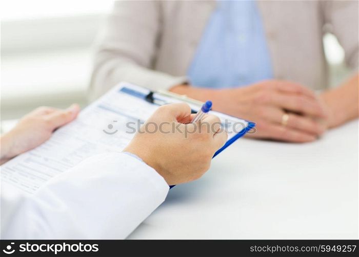 medicine, age, health care and people concept - close up of senior woman and doctor hands with clipboard meeting in medical office
