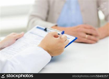 medicine, age, health care and people concept - close up of senior woman and doctor hands with clipboard meeting in medical office