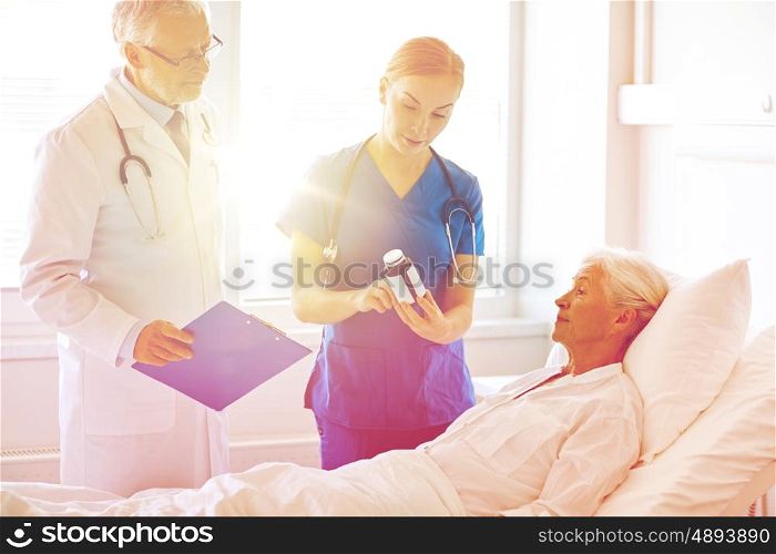 medicine, age, health care and people concept - doctor and nurse showing medicine to senior woman at hospital ward