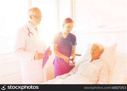 medicine, age, health care and people concept - doctor and nurse showing medicine to senior woman at hospital ward. doctor giving medicine to senior woman at hospital