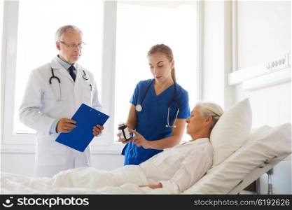 medicine, age, health care and people concept - doctor and nurse showing medicine to senior woman at hospital ward