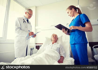 medicine, age, health care and people concept - doctor and nurse with clipboards visiting senior patient woman at hospital ward