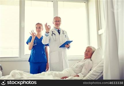 medicine, age, health care and people concept - doctor and nurse with tablet pc computer visiting senior patient woman and showing ok sign at hospital ward