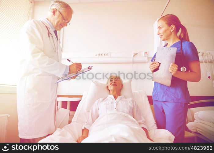 medicine, age, health care and people concept - doctor and nurse with clipboards visiting senior patient woman at hospital ward