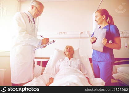 medicine, age, health care and people concept - doctor and nurse with clipboards visiting senior patient woman at hospital ward