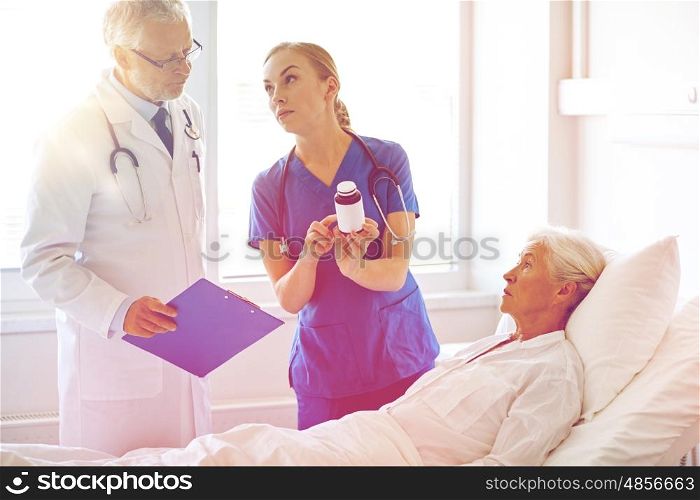 medicine, age, health care and people concept - doctor and nurse with medicine and senior woman at hospital ward