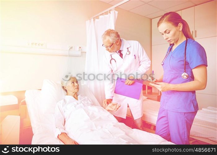 medicine, age, health care and people concept - doctor and nurse with clipboards visiting senior patient woman and checking her pulse at hospital ward