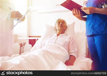 medicine, age, health care and people concept - doctor and nurse with clipboards visiting senior patient woman at hospital ward