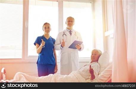 medicine, age, health care and people concept - doctor and nurse with tablet pc computer visiting senior patient woman and showing thumbs up at hospital ward. doctor and nurse visiting senior woman at hospital
