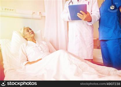 medicine, age, health care and people concept - doctor and nurse with tablet pc computer visiting senior patient woman at hospital ward. doctor and nurse visiting senior woman at hospital