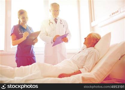 medicine, age, health care and people concept - doctor and nurse with clipboards visiting senior patient woman at hospital ward. doctor and nurse visiting senior woman at hospital
