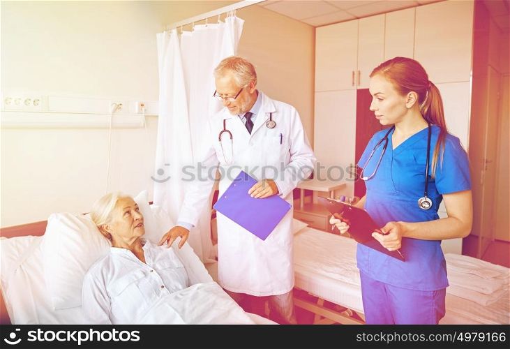 medicine, age, health care and people concept - doctor and nurse with clipboards visiting senior patient woman at hospital ward. doctor and nurse visiting senior woman at hospital
