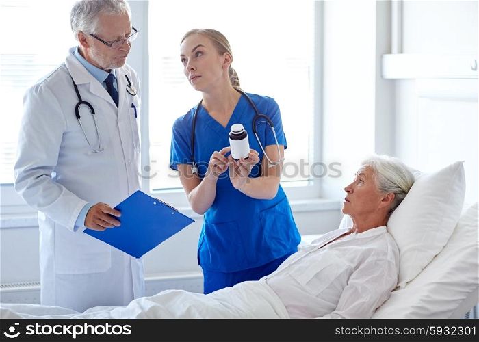 medicine, age, health care and people concept - doctor and nurse with medicine and senior woman at hospital ward