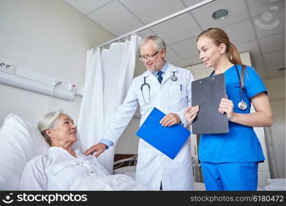 medicine, age, health care and people concept - doctor and nurse with clipboards visiting senior patient woman at hospital ward