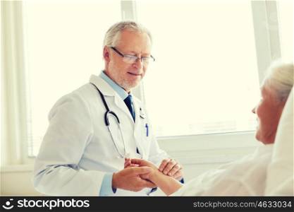 medicine, age, health care and people concept - doctor checking senior woman pulse at hospital ward