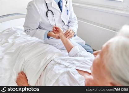 medicine, age, health care and people concept - doctor checking senior woman pulse at hospital ward. doctor checking senior woman pulse at hospital