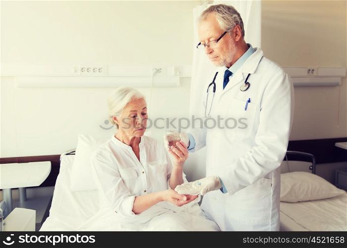 medicine, age, health care and people concept - doctor giving medication and water to senior woman at hospital ward