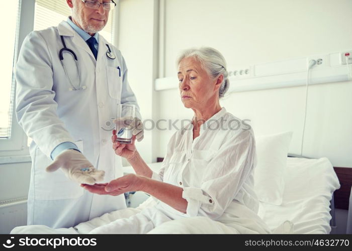 medicine, age, health care and people concept - doctor giving medication and water to senior woman at hospital ward