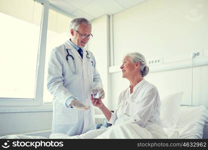 medicine, age, health care and people concept - doctor giving medication and water to senior woman at hospital ward