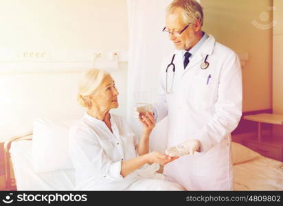 medicine, age, health care and people concept - doctor giving medication and water to senior woman at hospital ward