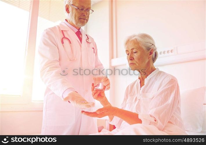 medicine, age, health care and people concept - doctor giving medication and water to senior woman at hospital ward