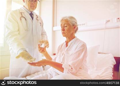 medicine, age, health care and people concept - doctor giving medication and water to senior woman at hospital ward. doctor giving medicine to senior woman at hospital