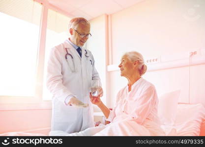 medicine, age, health care and people concept - doctor giving medication and water to senior woman at hospital ward. doctor giving medicine to senior woman at hospital