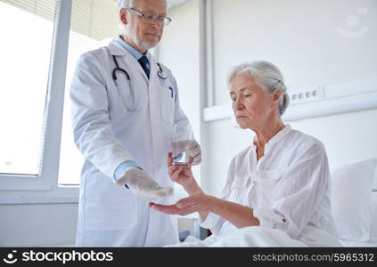 medicine, age, health care and people concept - doctor giving medication and water to senior woman at hospital ward