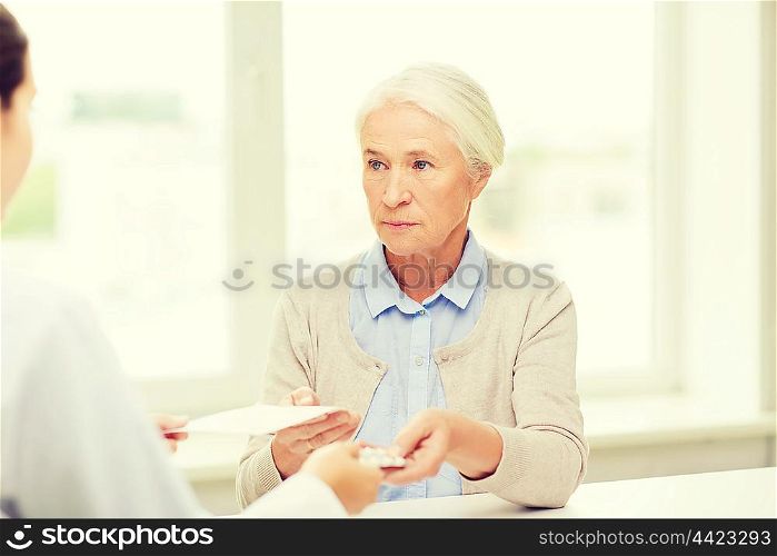 medicine, age, health care and people concept - doctor giving prescription and pills to senior woman at hospital