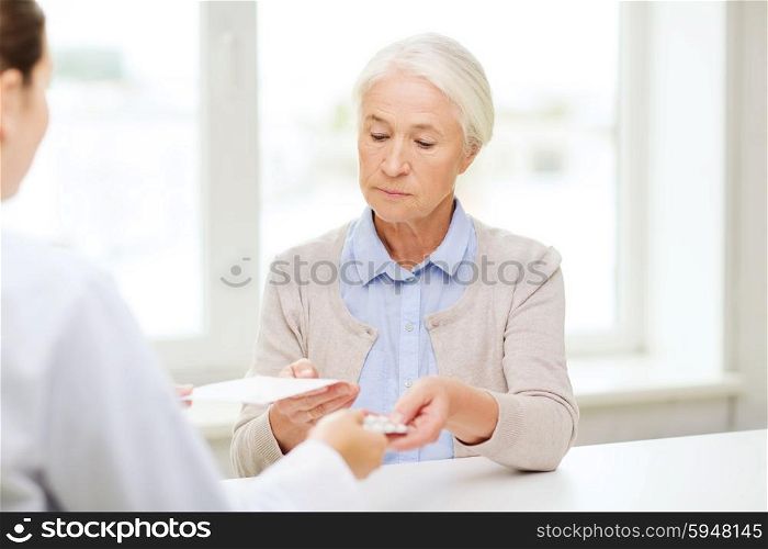 medicine, age, health care and people concept - doctor giving prescription and pills to senior woman at hospital