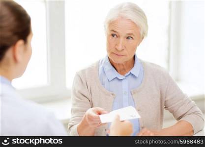 medicine, age, health care and people concept - doctor giving prescription to senior woman at hospital