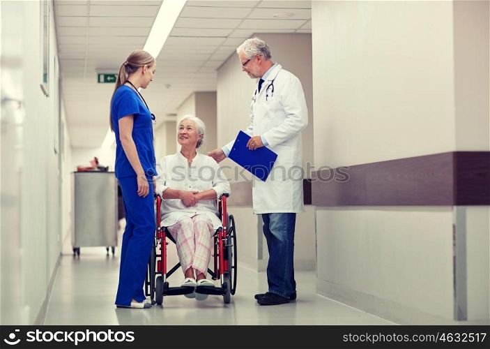 medicine, age, health care and people concept - doctor, nurse and senior woman patient in wheelchair at hospital corridor