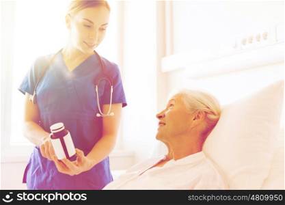 medicine, age, health care and people concept - doctor or nurse showing medicine to senior woman at hospital ward
