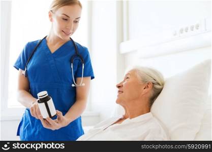medicine, age, health care and people concept - doctor or nurse showing medicine to senior woman at hospital ward