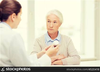 medicine, age, health care and people concept - doctor showing pills to senior woman at hospital