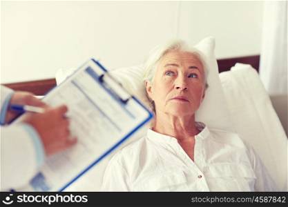 medicine, age, health care and people concept - doctor with clipboard visiting senior woman at hospital ward