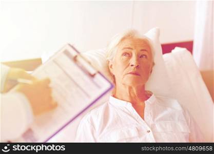 medicine, age, health care and people concept - doctor with clipboard visiting senior woman at hospital ward