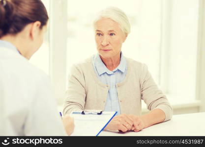 medicine, age, health care and people concept - doctor with clipboard writing prescription for senior woman at hospital